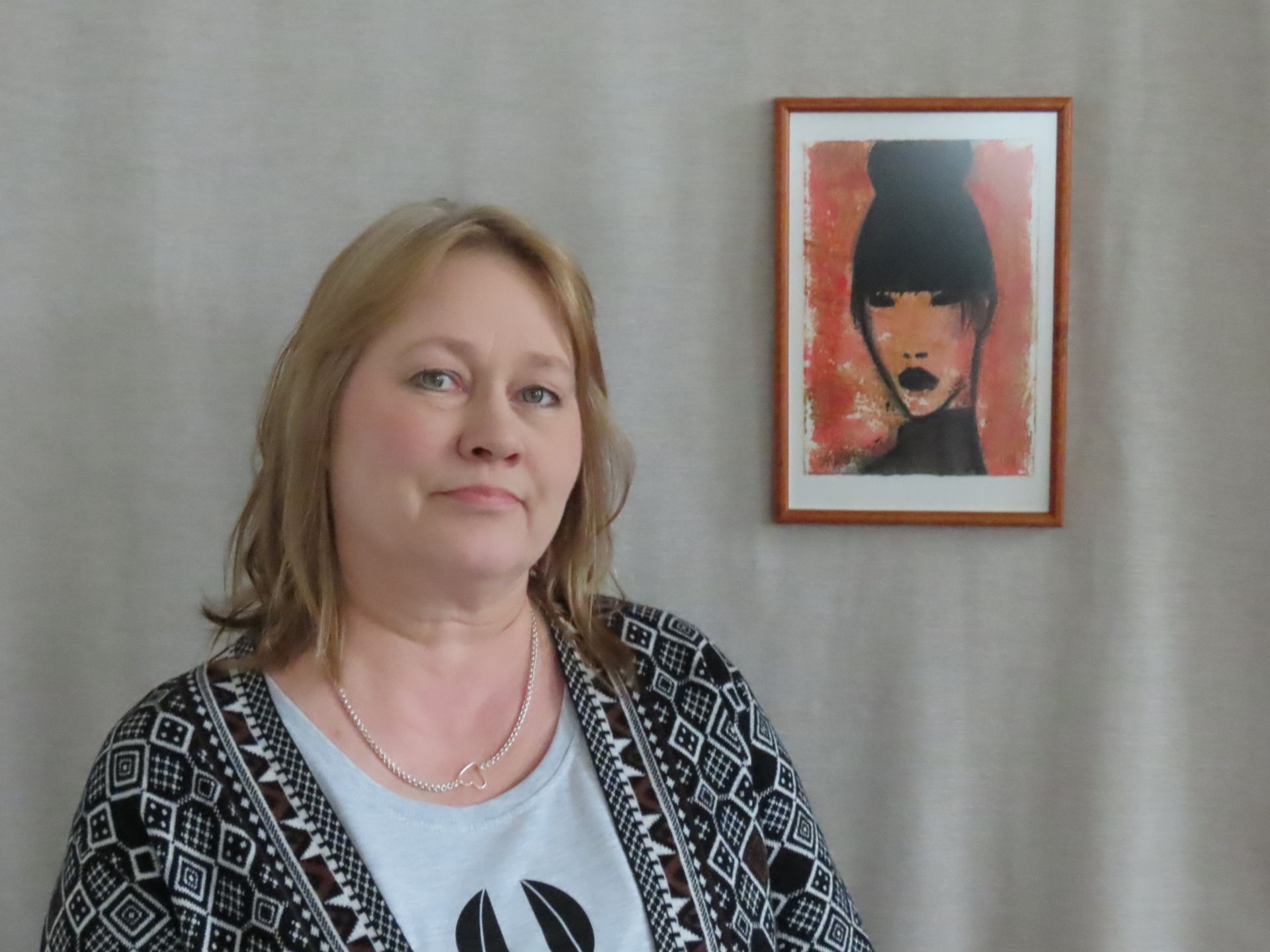 Artist Helena Junttila next to a portrait, in black ink with a red background, of a person.