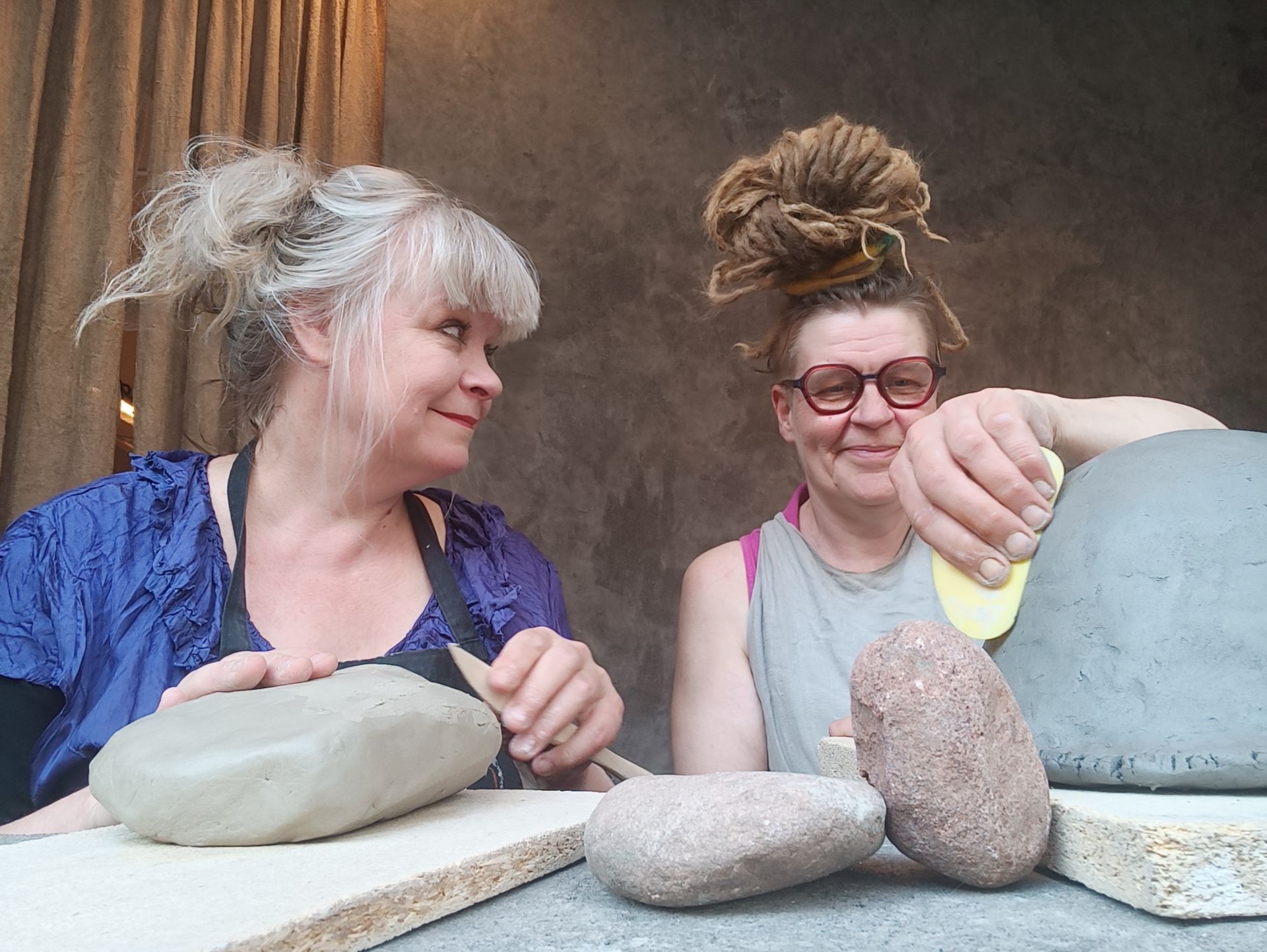 two women sitting behind big lumps of clay