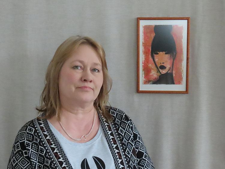 Taiteilija Helena Junttila, valokuva naisesta maalatun muotokuvan vieressä