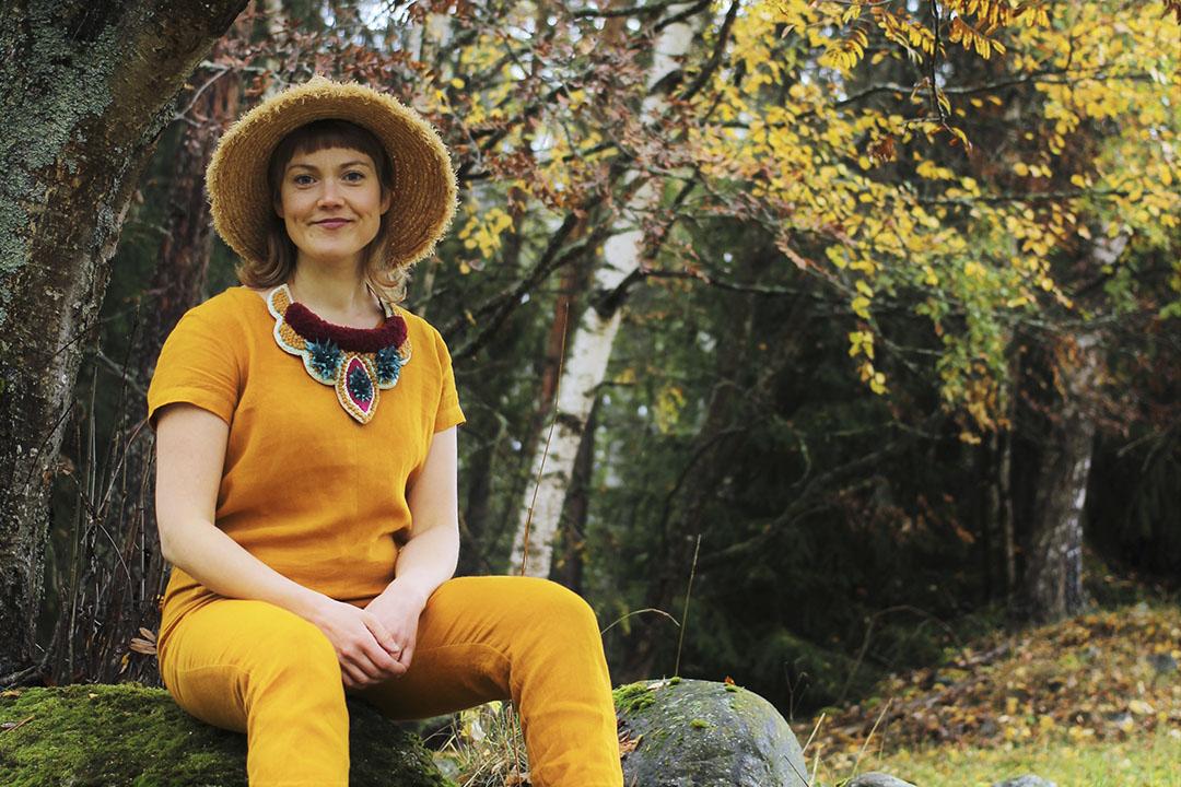 Artist Alexandra Lindqvist sitting on a rock in a yellow outfit